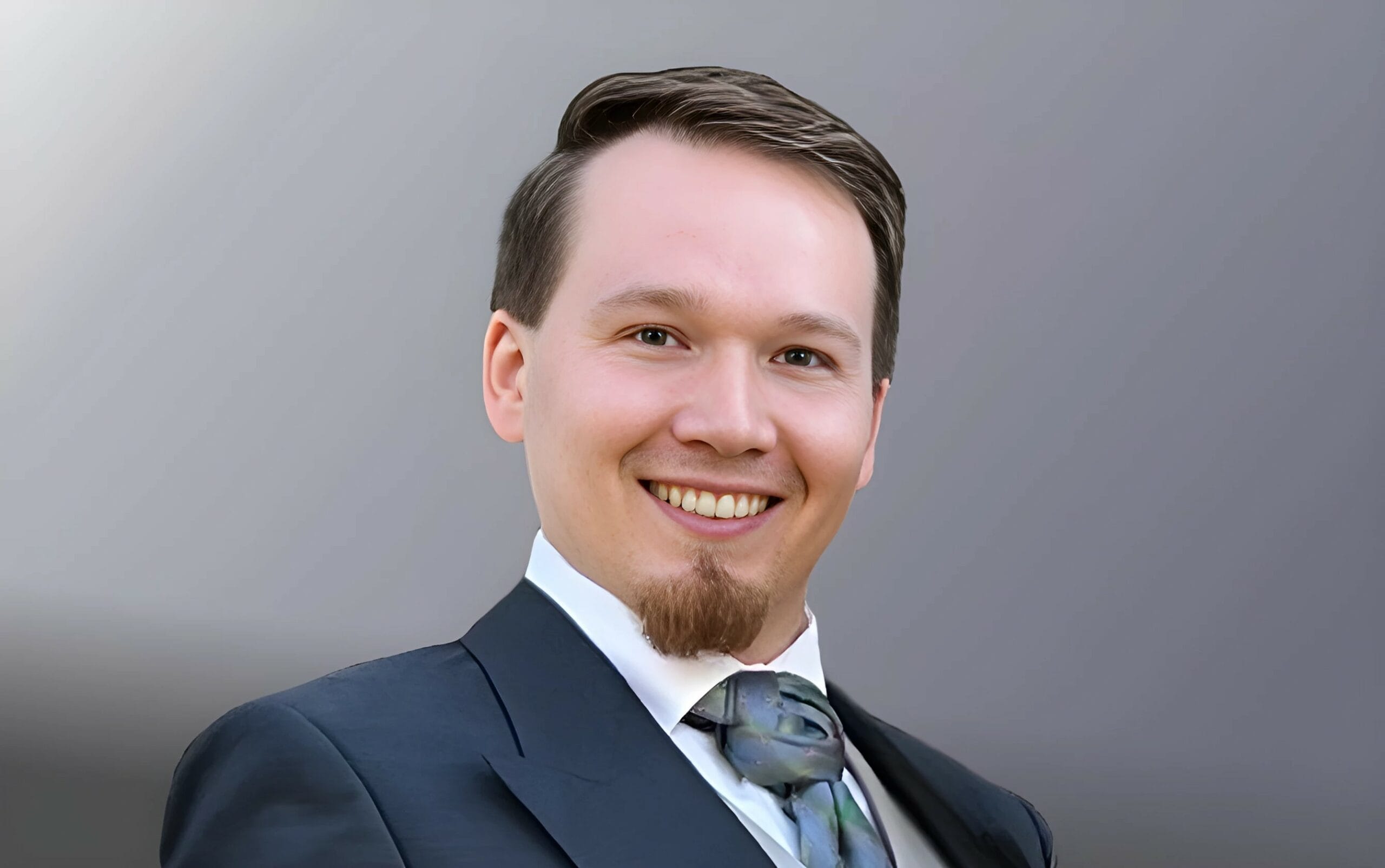 Porträt von Robert Skawinski, ein lächelnder Mann im Anzug mit Krawatte vor neutralem Hintergrund.