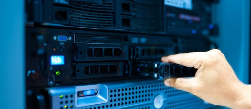 Hand eines IT-Technikers, der eine Festplatte in einen Server im Rechenzentrum einsetzt oder herausnimmt.