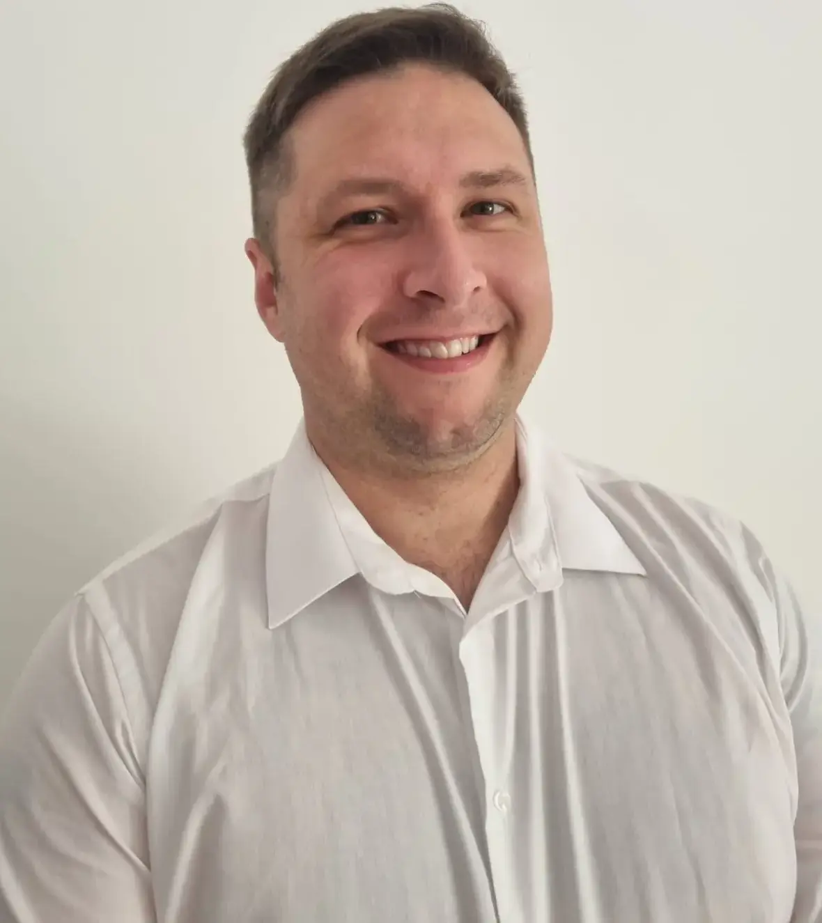 Porträt von Matthiew Rozenboom, ein lächelnder junger Mann mit kurzen Haaren, im weißen Hemd vor hellem, neutralem Hintergrund.
